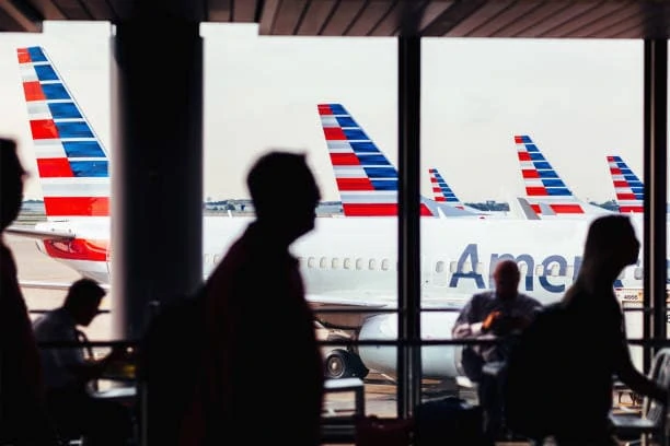 Passengers walking through a corridor with American Airlines planes in the Background